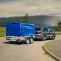 Szary SUV ciągnie dwuosiową przyczepę pod niebieską plandeką. Czy można ciągnąć przyczepę dwuosiową na kat. B?