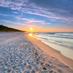 Zachód słońca nad morzem, piaszczysta plaża z śladami stóp, las w tle. Idealne, fajne miejsce nad morzem dla dwojga na romantyczny spacer.