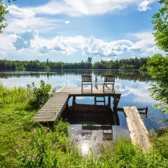 Idealne miejsce na camping Bory Tucholskie: pomost z krzesłami nad spokojnym jeziorem, otoczony zielenią.