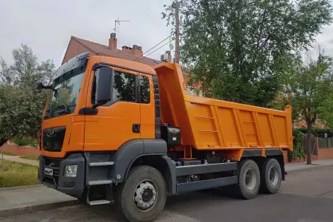 Pomarańczowa wywrotka, idealna do transportu materiałów budowlanych. Z kategorią C można ciągnąć taką przyczepę.