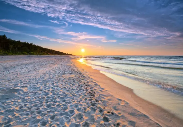 Zachód słońca nad morzem, piaszczysta plaża z śladami stóp, las w tle. Idealne, fajne miejsce nad morzem dla dwojga na romantyczny spacer.