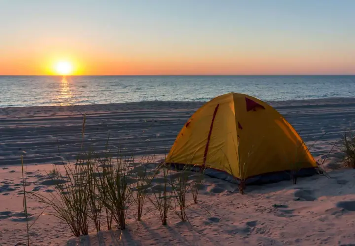 Żółty namiot na piaszczystej plaży, z widokiem na spokojne morze i zachodzące słońce. Idealne miejsce na nocleg, gdzie pole namiotowe nad morzem wita o poranku.