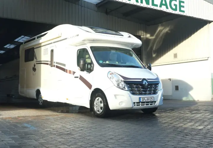 Biała kamperka "Alaska TD" wyjeżdża z hali, gotowa na targi caravaningowe.