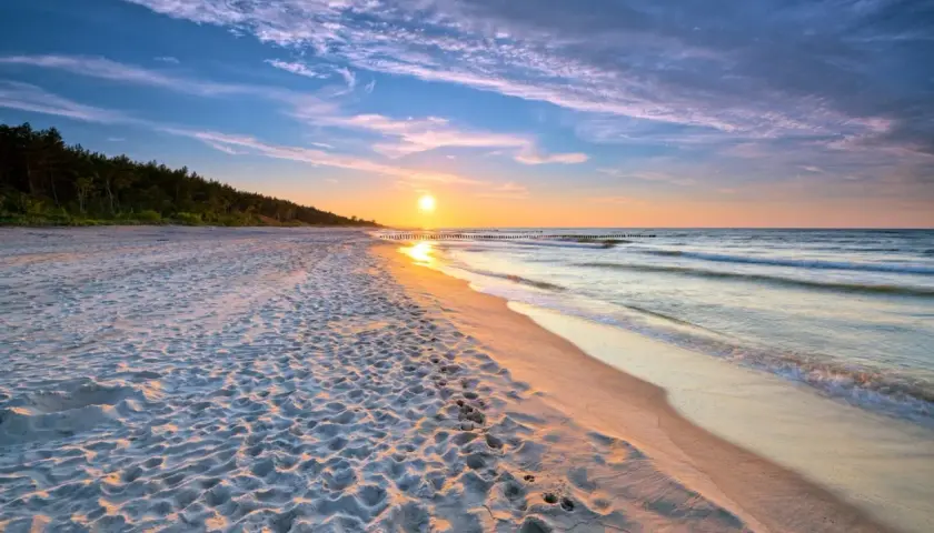 Zachód słońca nad morzem, piaszczysta plaża z śladami stóp, las w tle. Idealne, fajne miejsce nad morzem dla dwojga na romantyczny spacer.