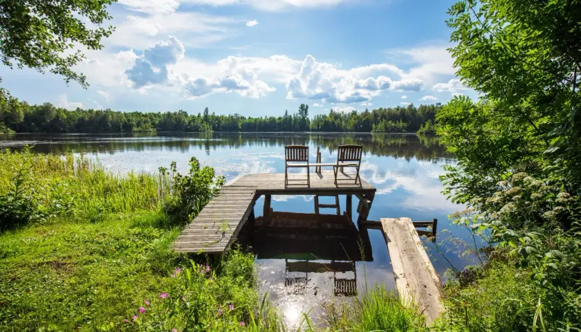Idealne miejsce na camping Bory Tucholskie: pomost z krzesłami nad spokojnym jeziorem, otoczony zielenią.