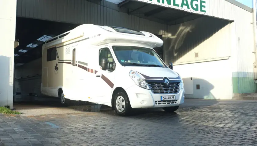 Biała kamperka "Alaska TD" wyjeżdża z hali, gotowa na targi caravaningowe.