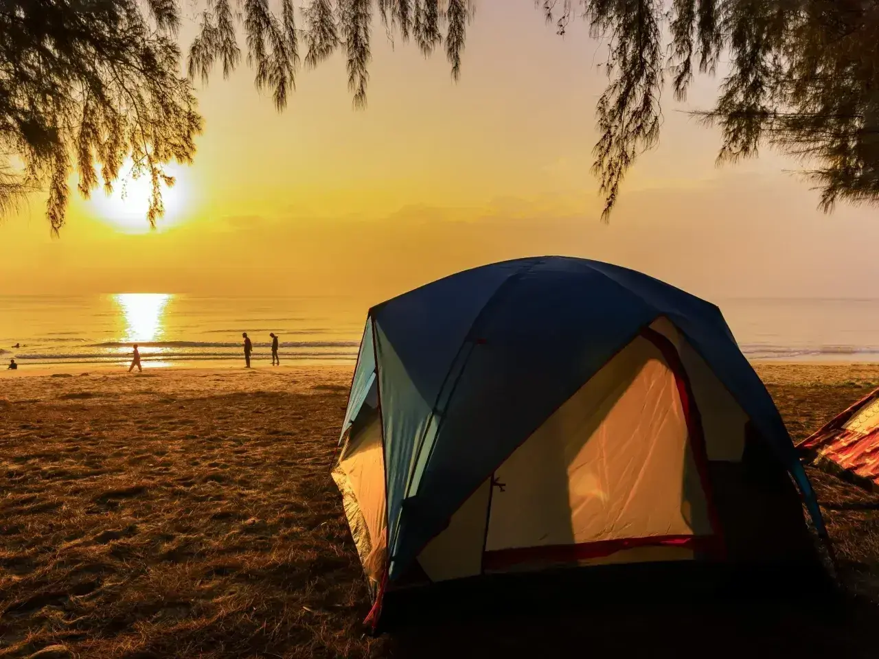 Wschód słońca nad morzem, gdzie rozbito luksusowe pole namiotowe. Ludzie spacerują po plaży, a namioty kuszą komfortem.