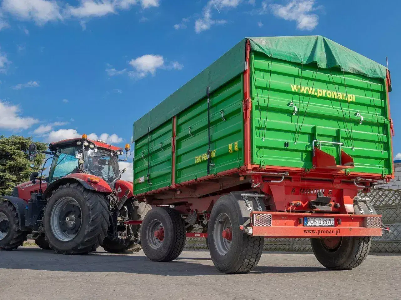 Czerwony traktor ciągnie zieloną przyczepę z plandeką. Duża masa przyczepy gotowa do pracy na polu.