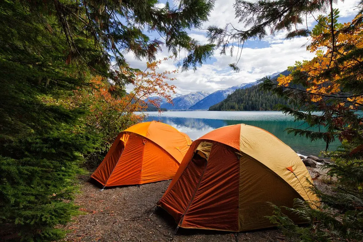 Dwa pomarańczowe namioty na brzegu jeziora, otoczone jesiennymi drzewami. Idealne miejsce na camping Jastrzębia Góra.