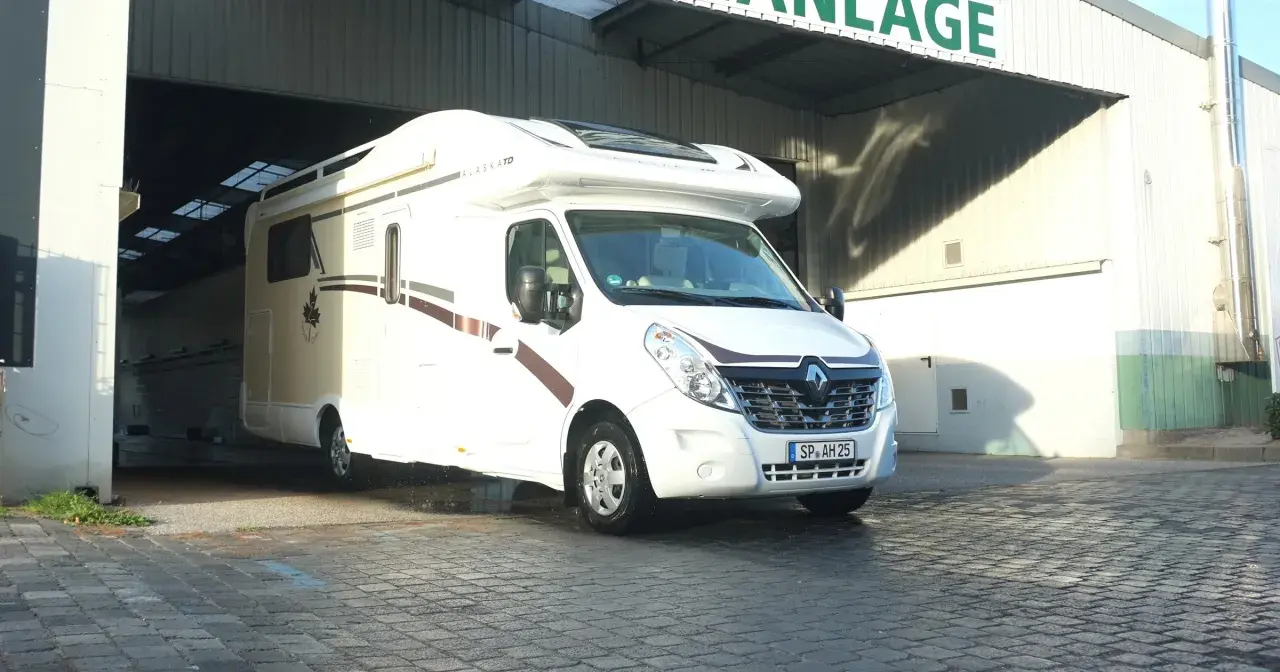 Biała kamperka "Alaska TD" wyjeżdża z hali, gotowa na targi caravaningowe.