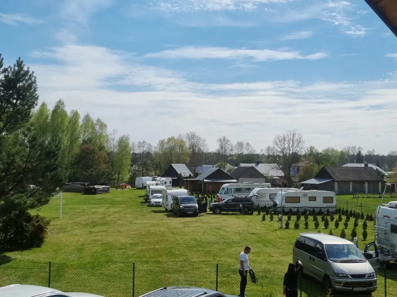 Urokliwy camping Roztocze z przyczepami kempingowymi i kamperami na zielonej trawie, pod błękitnym niebem z chmurami.