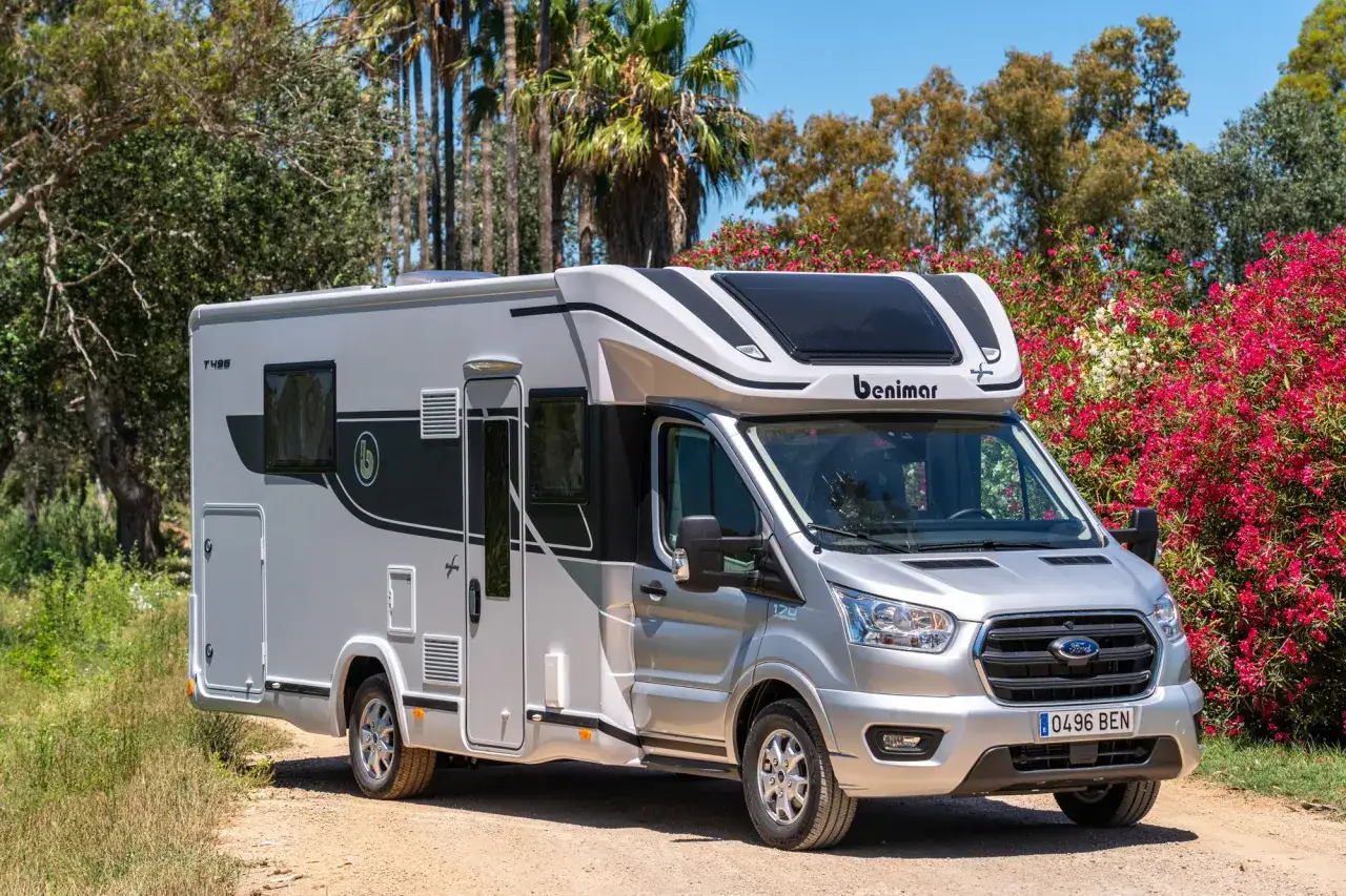 Kamper Ford Benimar T496 zaparkowany na drodze wśr&oacute;d zieleni i kwitnących krzew&oacute;w.