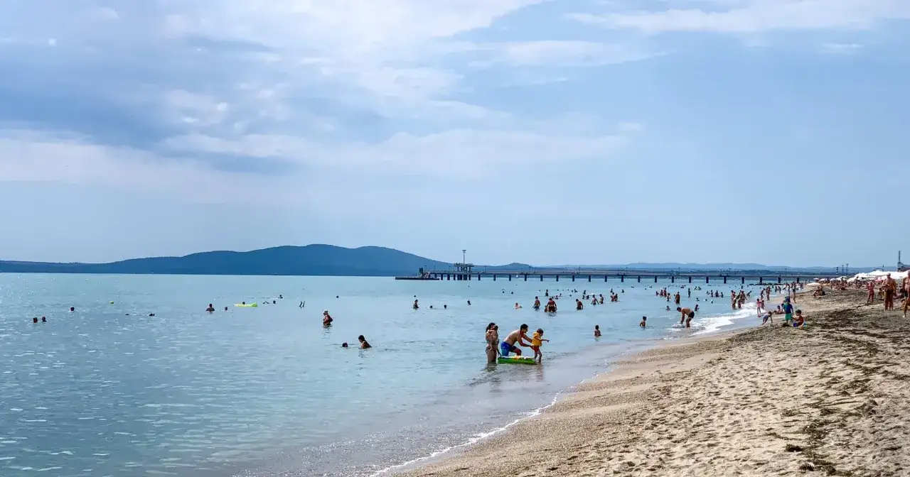 Ludzie kąpią się i opalają na plaży w Burgas. Czy warto tu przyjechać? Woda jest spokojna, a widok na molo zachęca do relaksu.