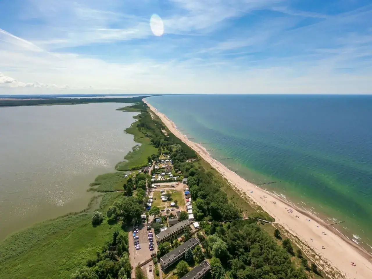 Malowniczy widok na pole namiotowe nad morzem, z jednej strony jezioro, z drugiej plaża i błękitne morze.